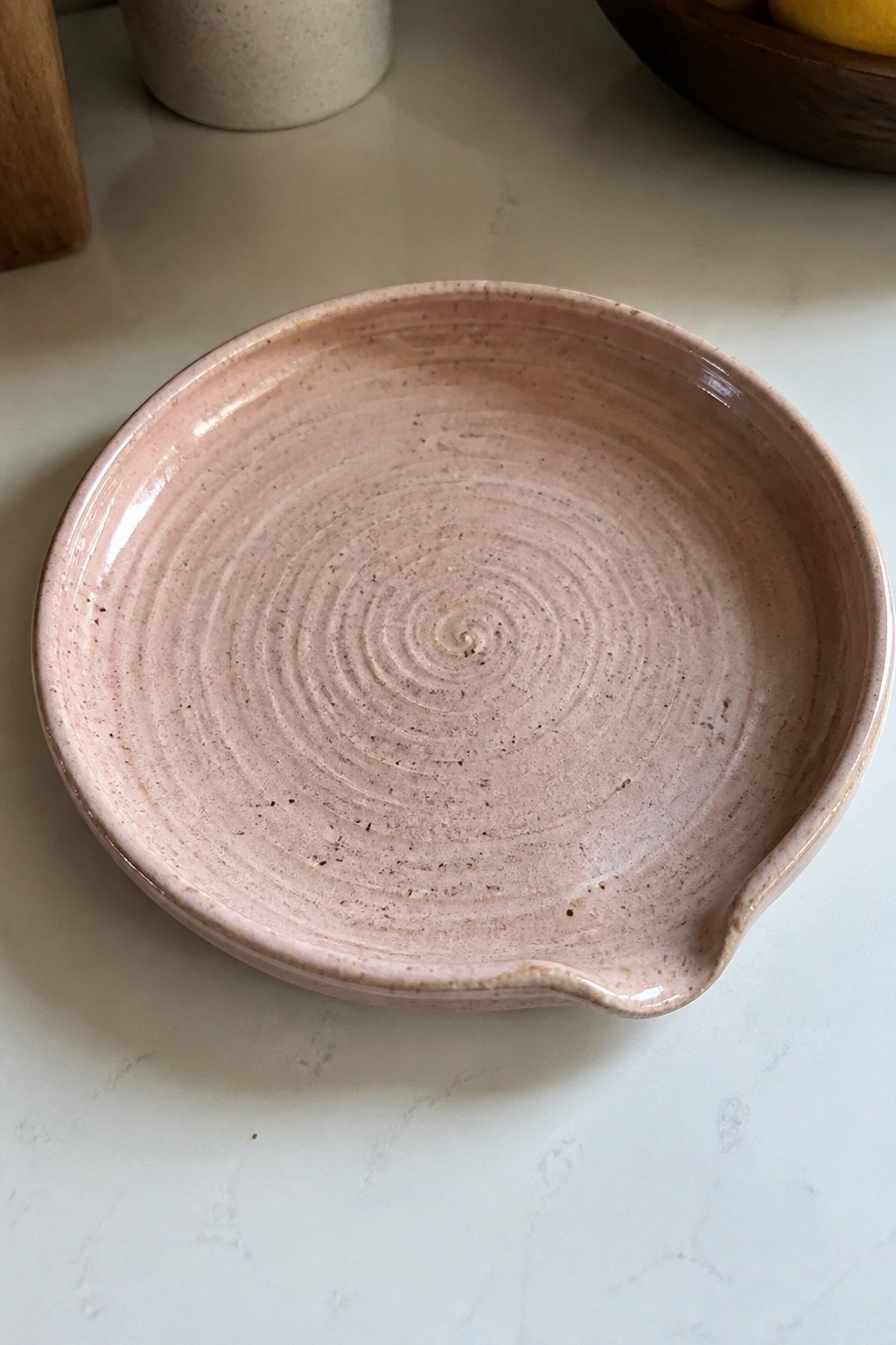Pink speckled ceramic plate with spiral grooves and pouring spout on white counter