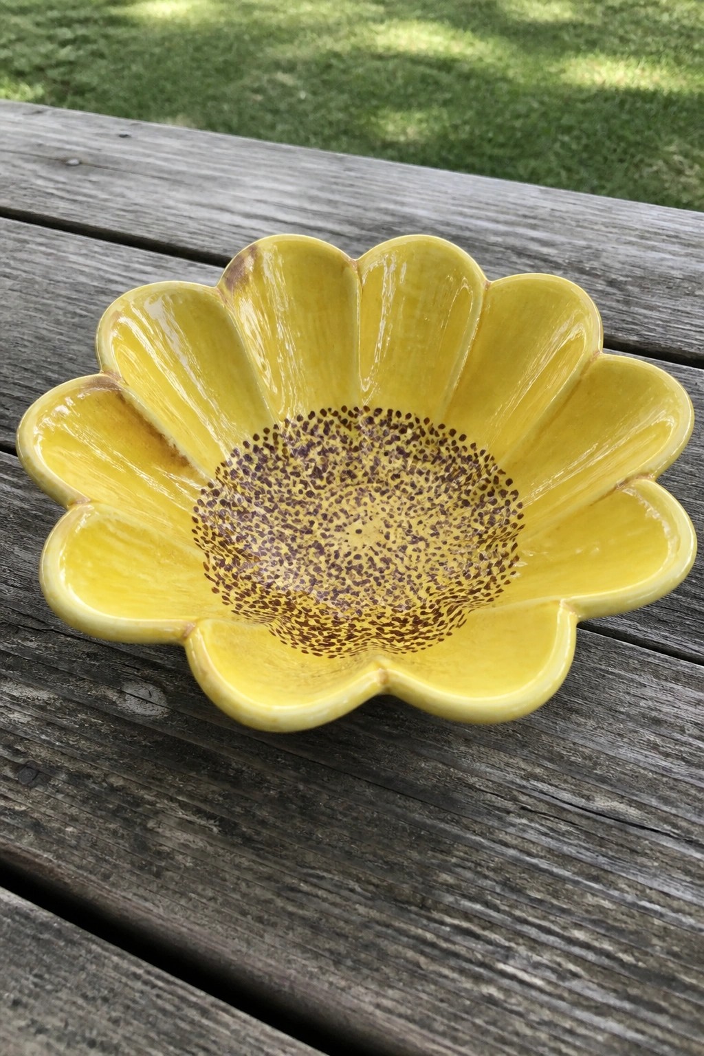 Yellow flower-shaped ceramic bowl with brown speckled center on wooden table
