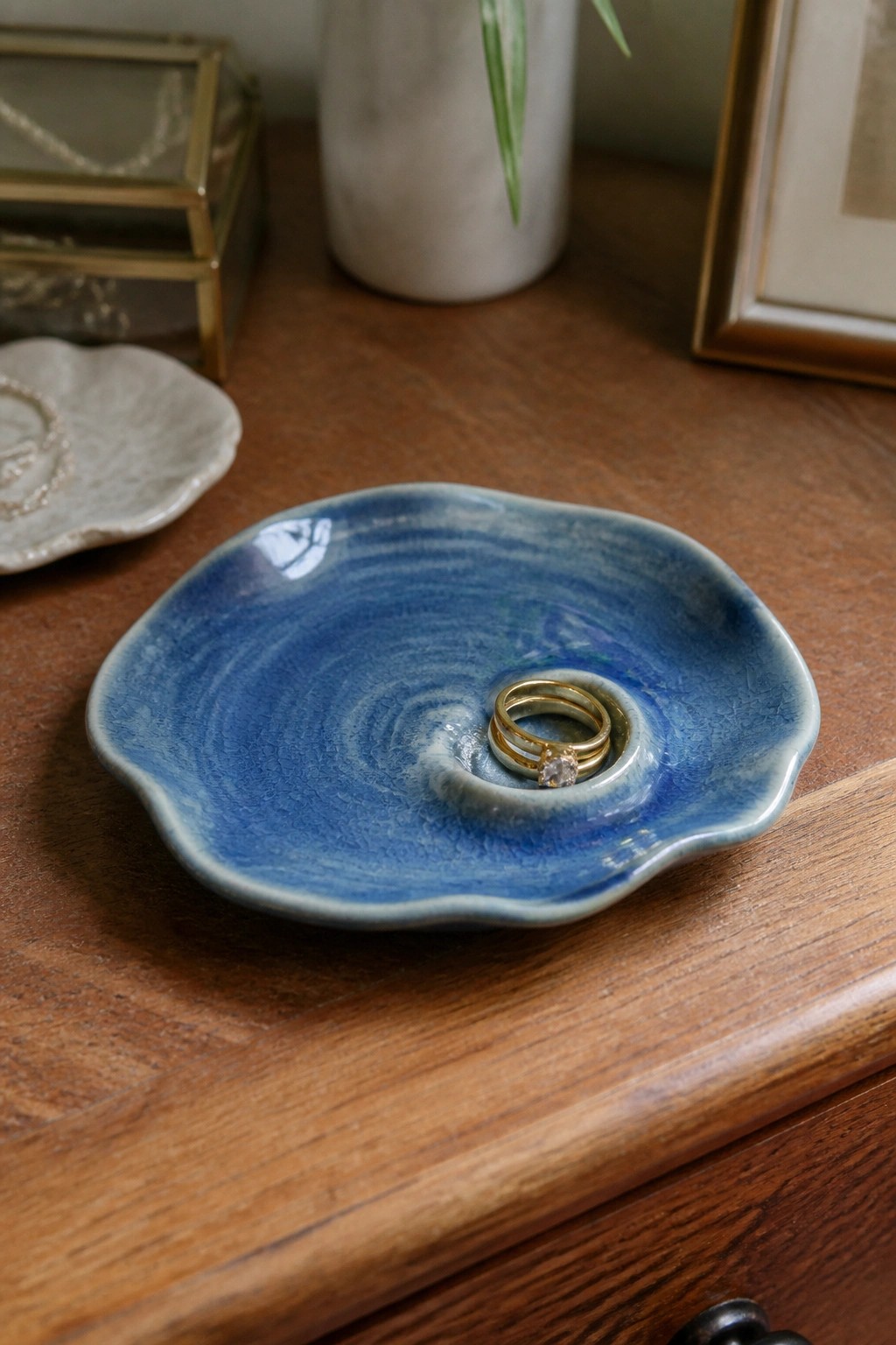 Blue swirled ceramic dish holding gold rings on wooden table surface