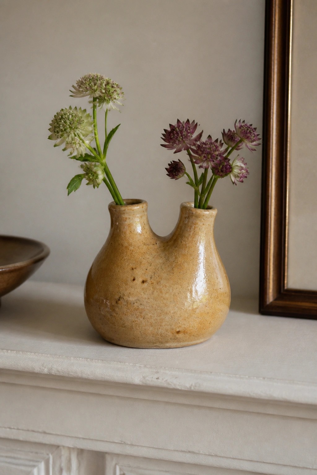 Beige double-neck ceramic vase with purple and white flowers on white mantel