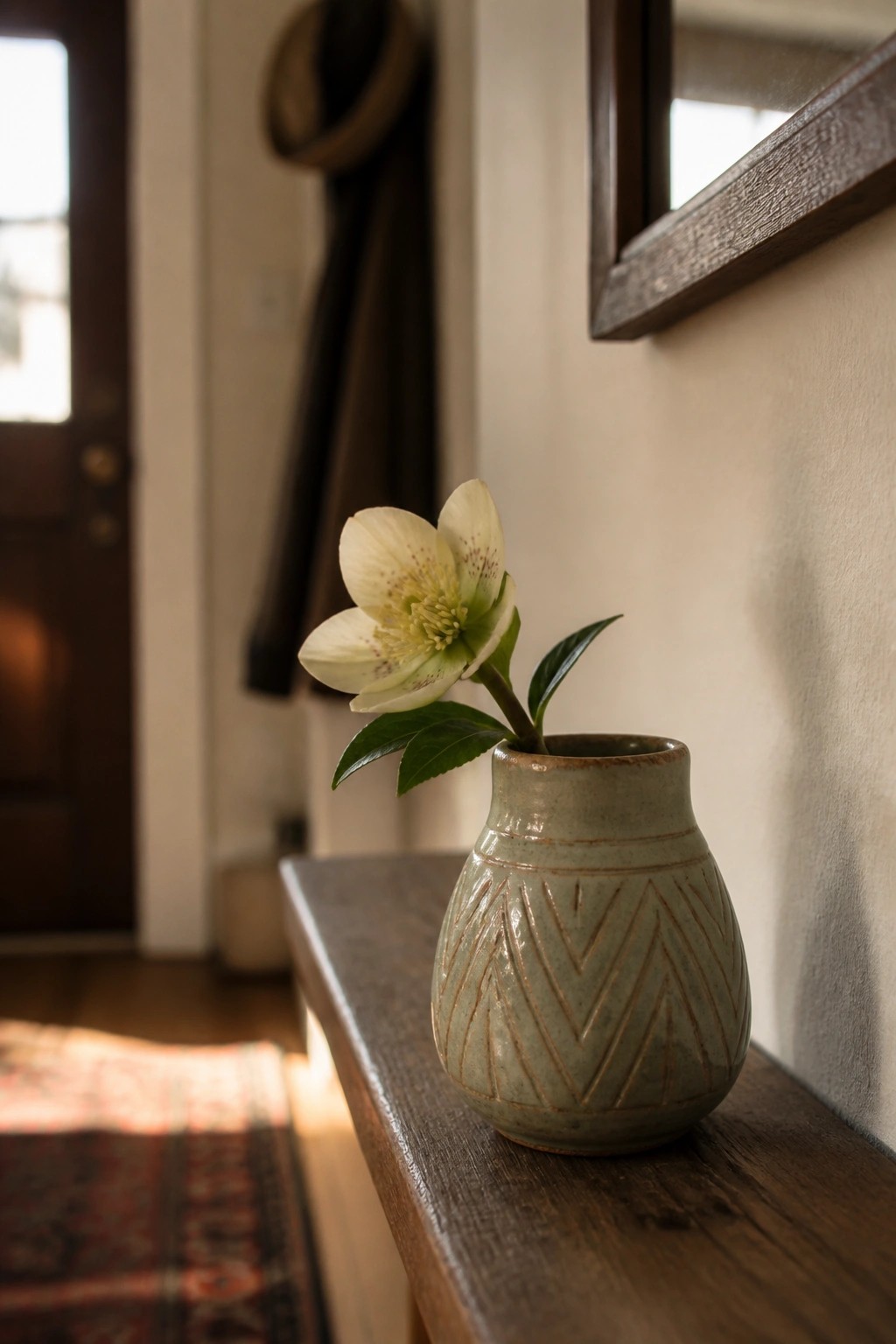 White hellebore flower in patterned sage-green vase on dark wooden bench