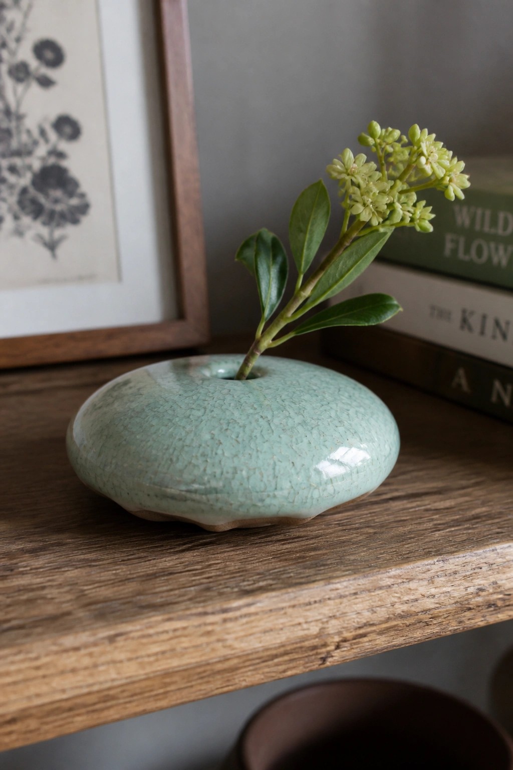 Light green crackled ceramic vase with small flowering plant on wooden shelf