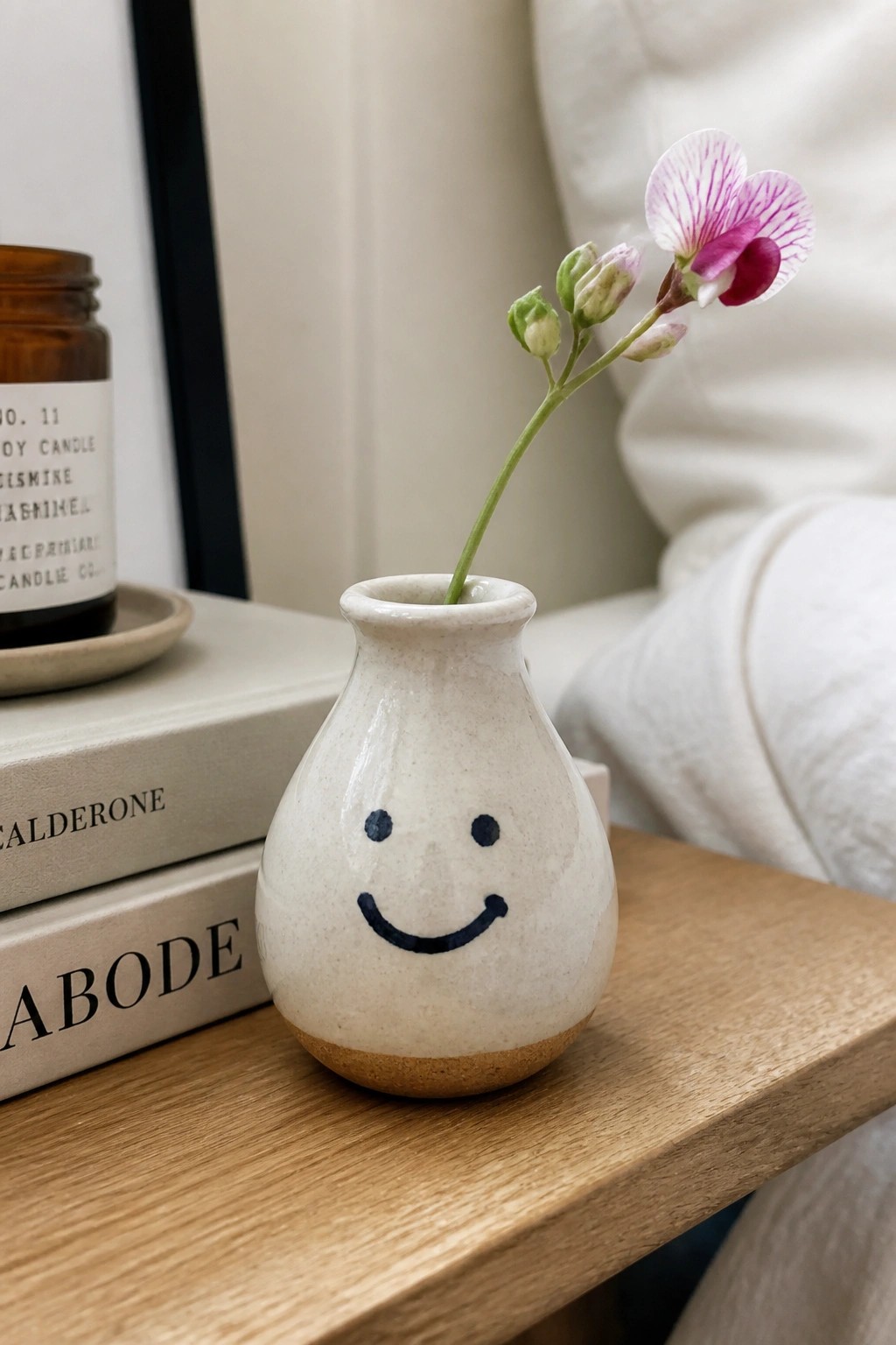 Smiley face vase with purple flower on wooden table beside stacked books