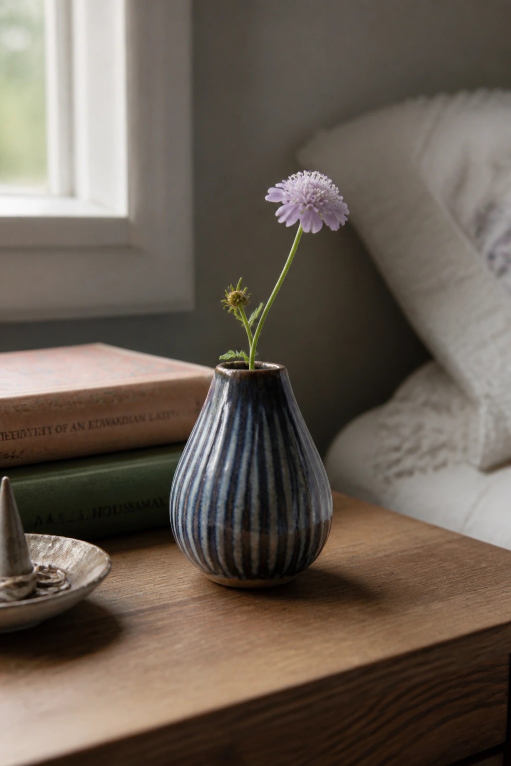 Blue striped vase with purple flower on wooden table beside stacked books