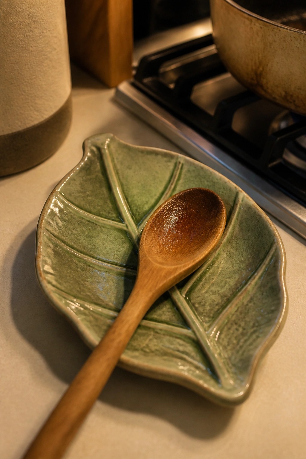 Wooden spoon resting on green leaf-shaped ceramic dish near stove