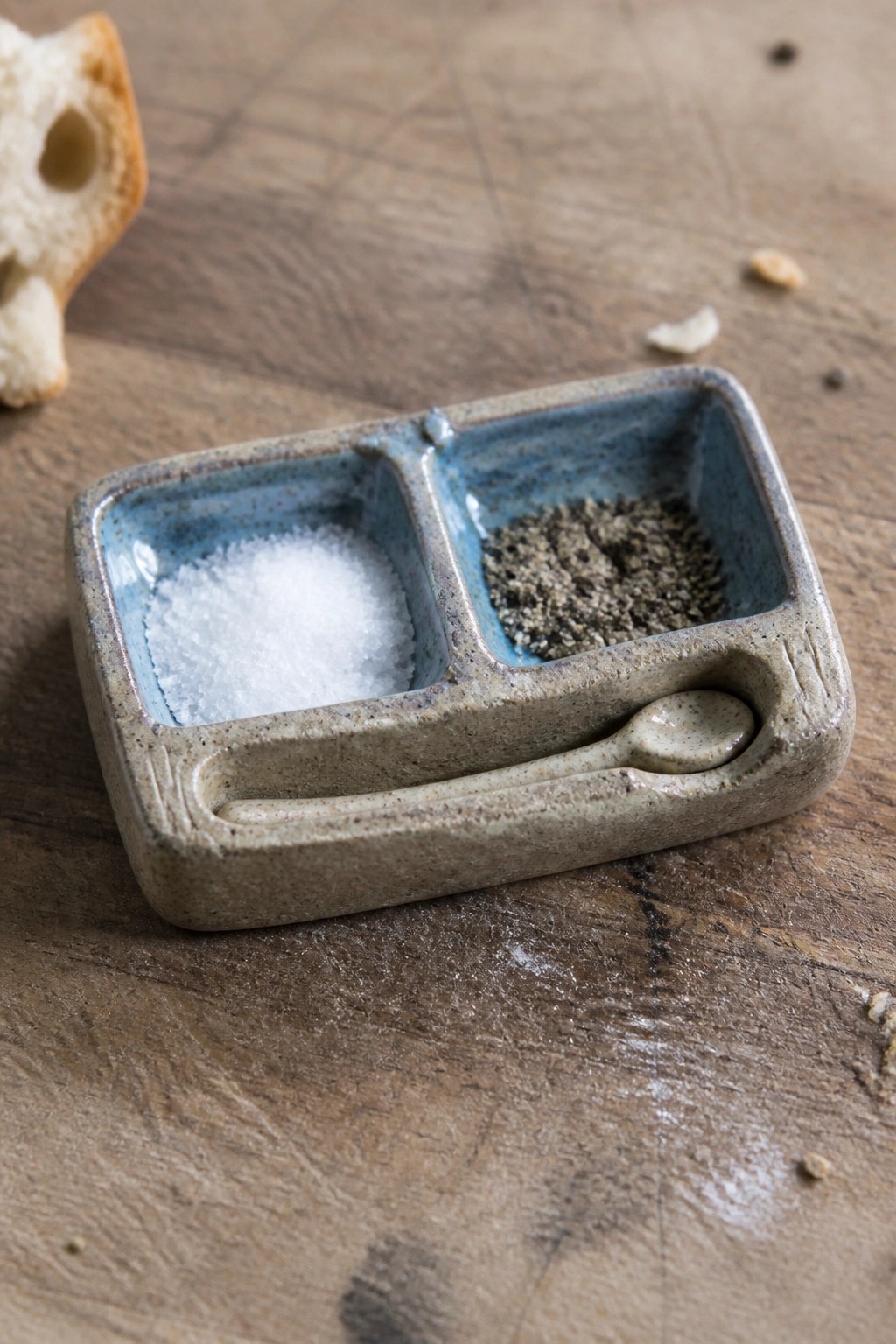 Ceramic salt and pepper dish with miniature spoon on wooden table