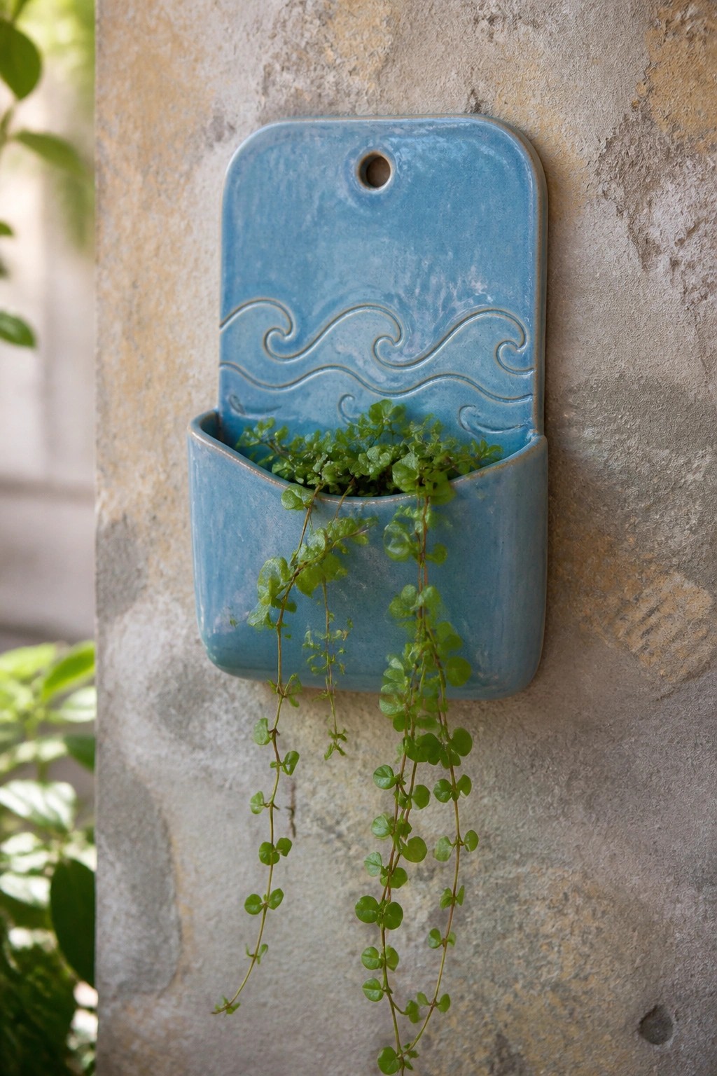 Blue ceramic wall planter with wave design and trailing green plant on stone wall.