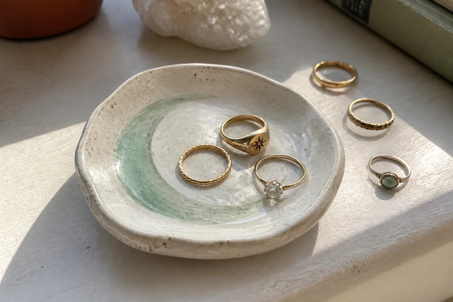 Assorted gold and silver rings in a moon-decorated ceramic dish on a windowsill.
