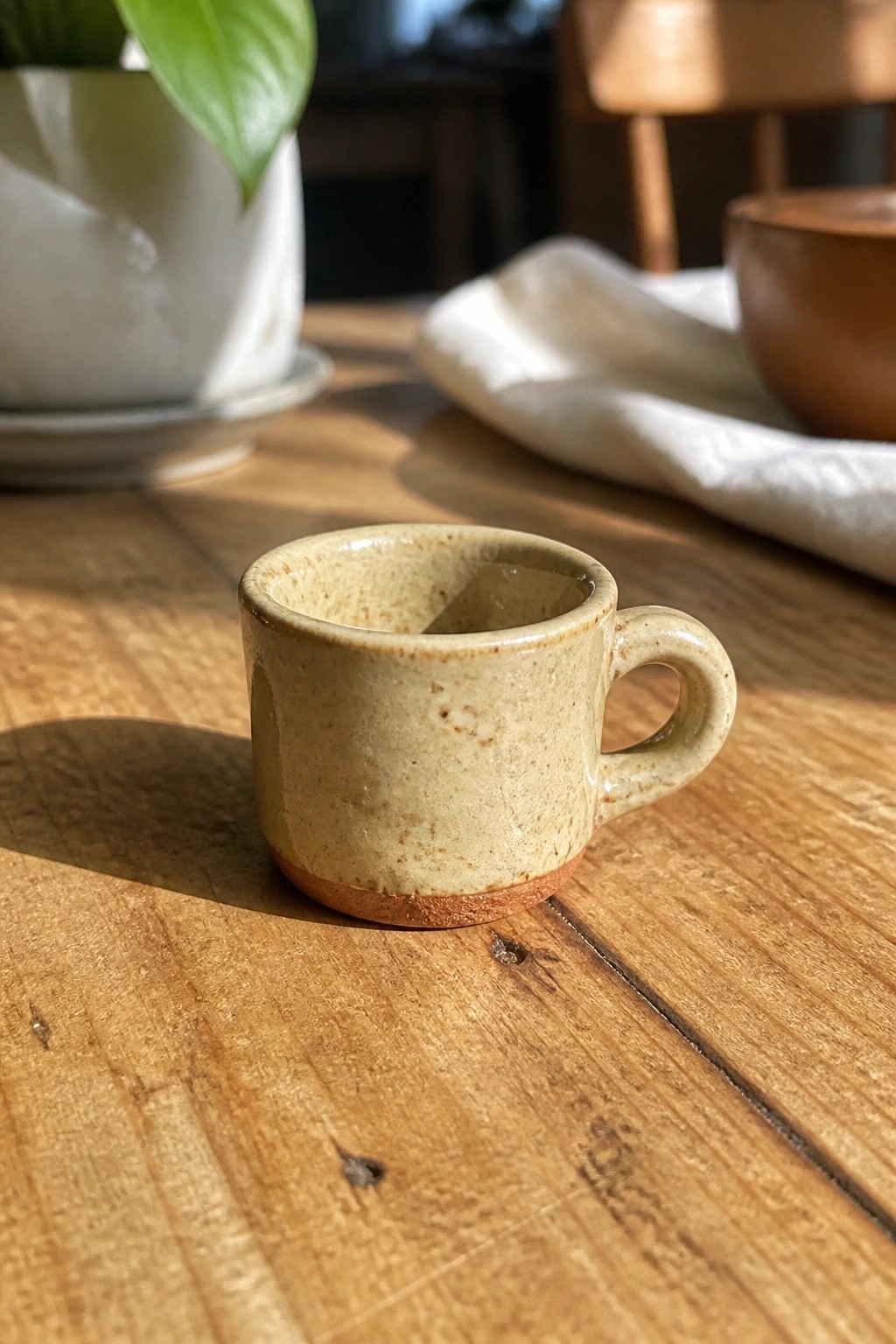 Small speckled beige ceramic mug with handle on sunlit wooden table