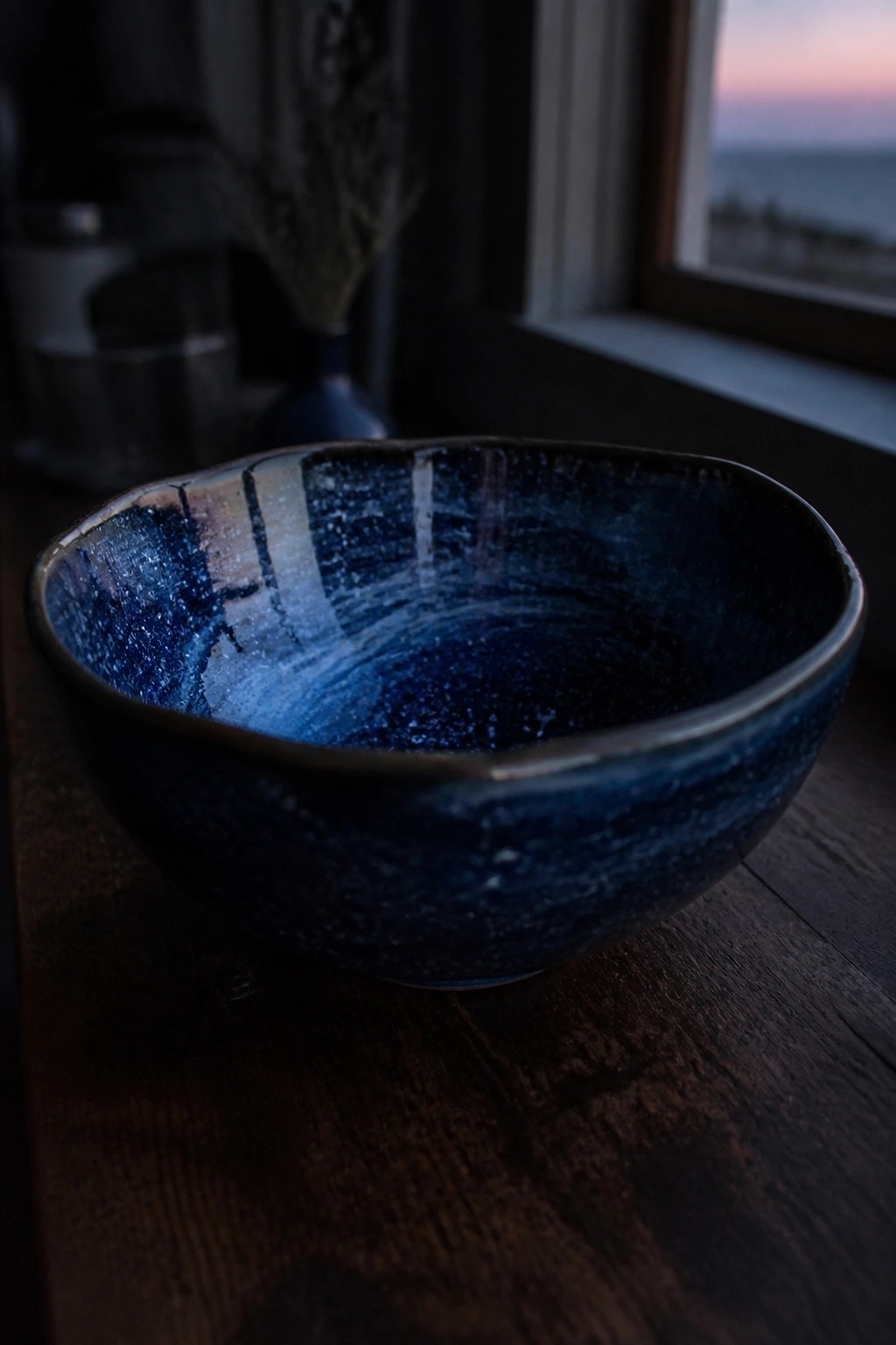 Speckled blue ceramic bowl on wooden table with ocean view at dusk