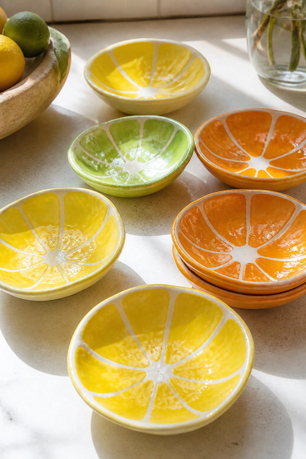 Vibrant ceramic bowls shaped like lemon, lime, and orange slices on a countertop.