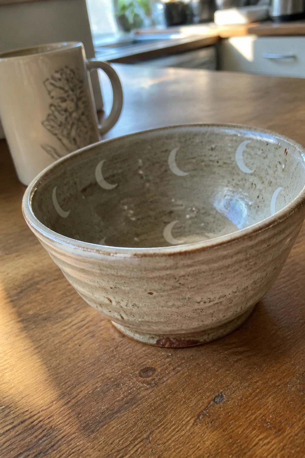 A speckled ceramic bowl with white crescent moons painted inside the rim sits on a wooden table.