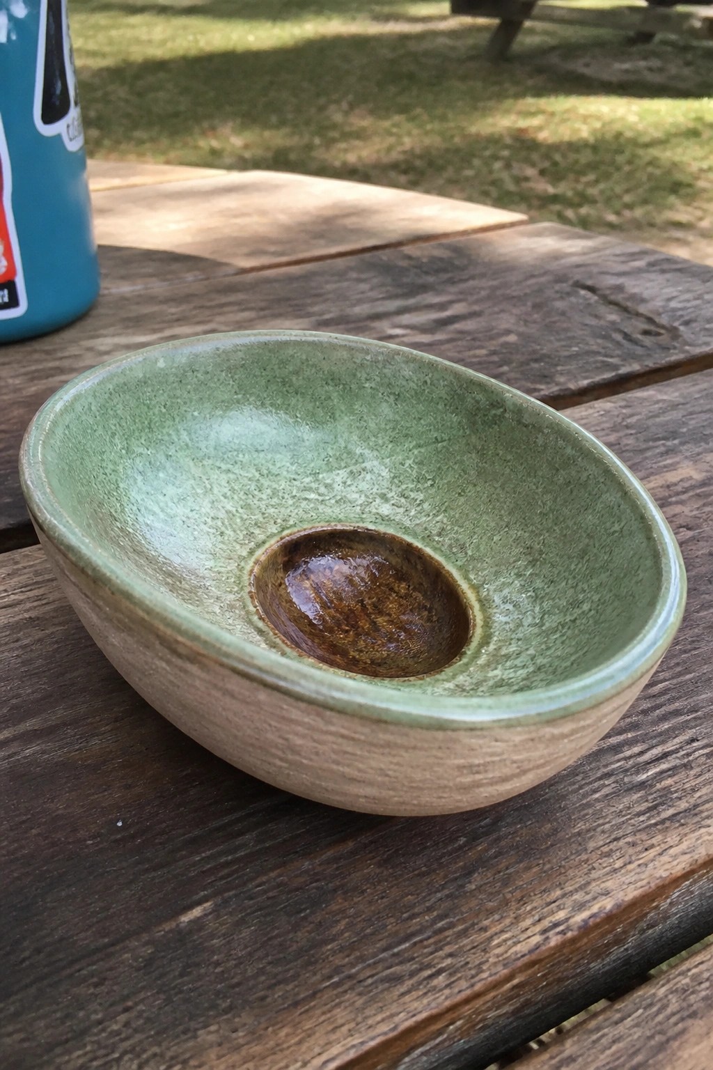 Green speckled ceramic bowl with brown center on wooden picnic table outdoors