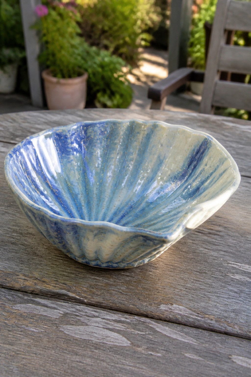 Blue scalloped ceramic bowl with radiating glaze on wooden outdoor table