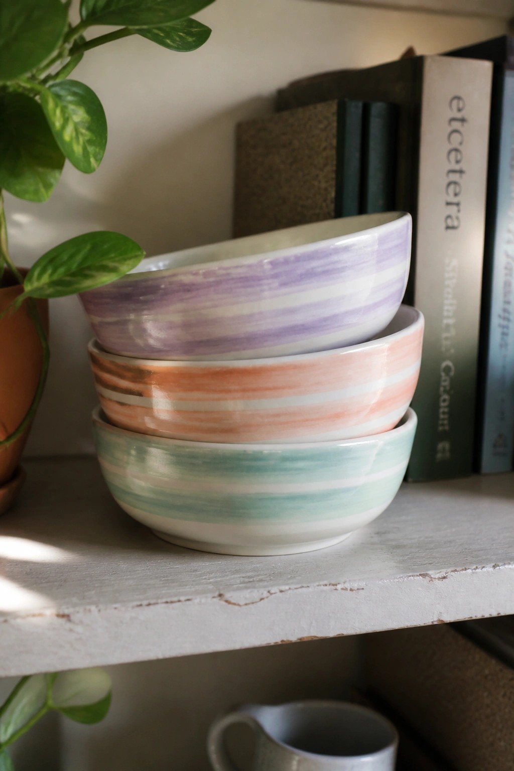 Stacked pastel striped bowls in purple, orange, and green on a shelf