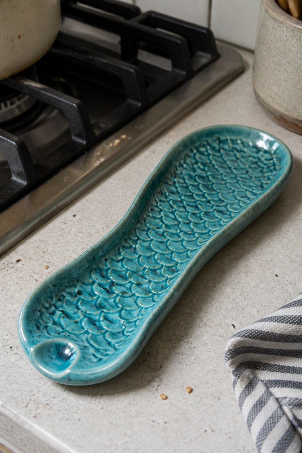 Teal ceramic spoon rest with fish-scale texture on kitchen counter near stove