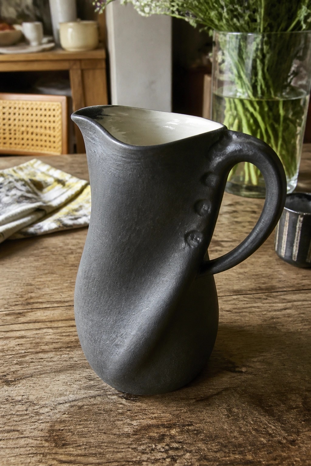 Black ceramic pitcher with dotted handle on rustic wooden table with greenery
