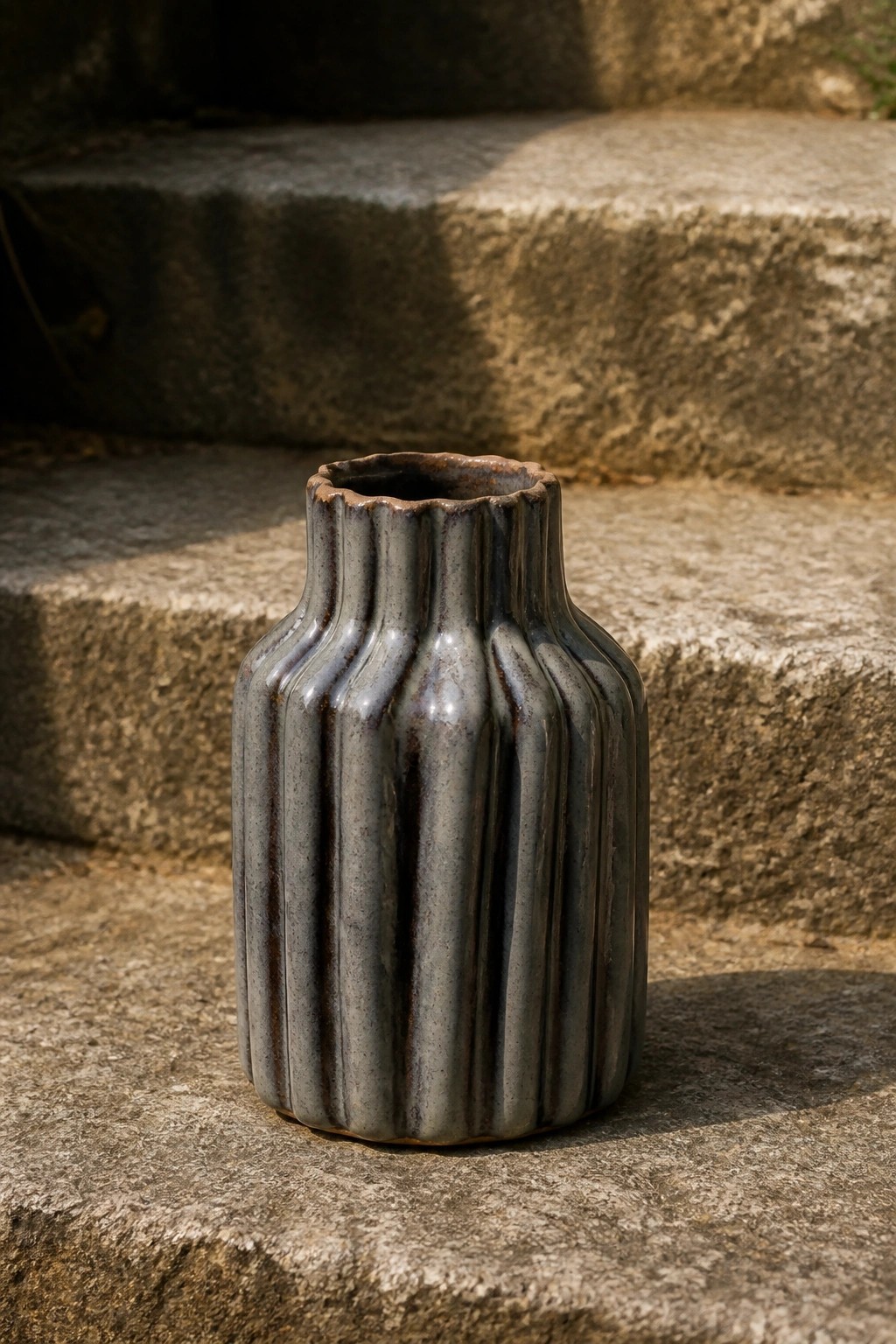 Ribbed gray ceramic vase with brown speckles on stone steps.