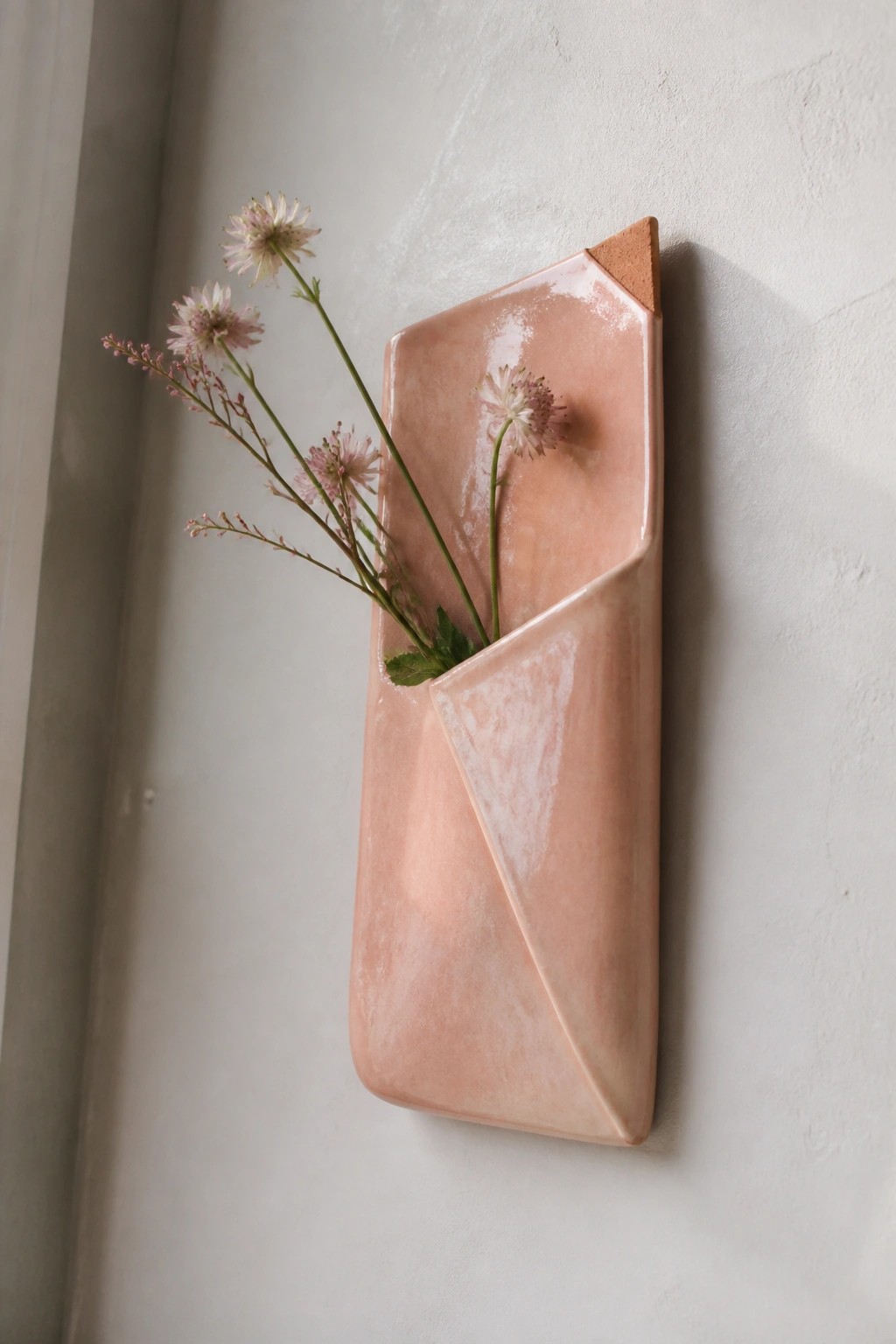 Pink ceramic geometric wall vase with wildflowers on textured white wall