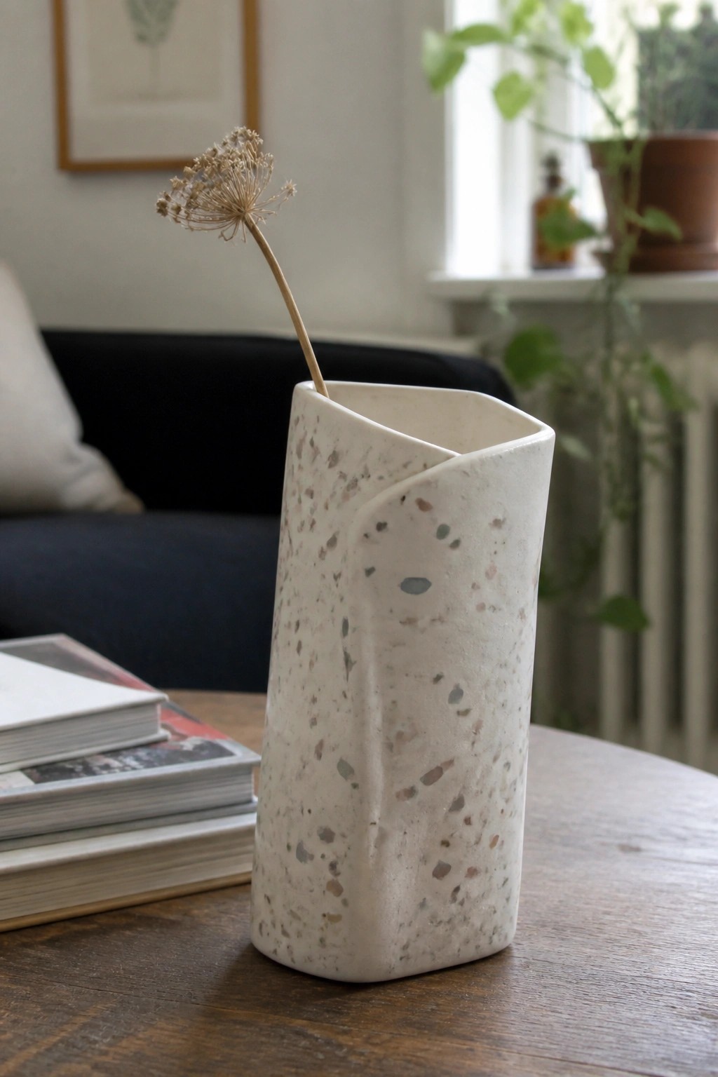 Speckled ceramic vase holding dried flower on wooden table with books nearby
