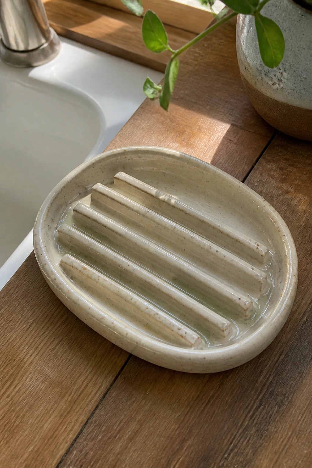 Oval speckled ceramic soap dish with ridges on wooden counter near sink