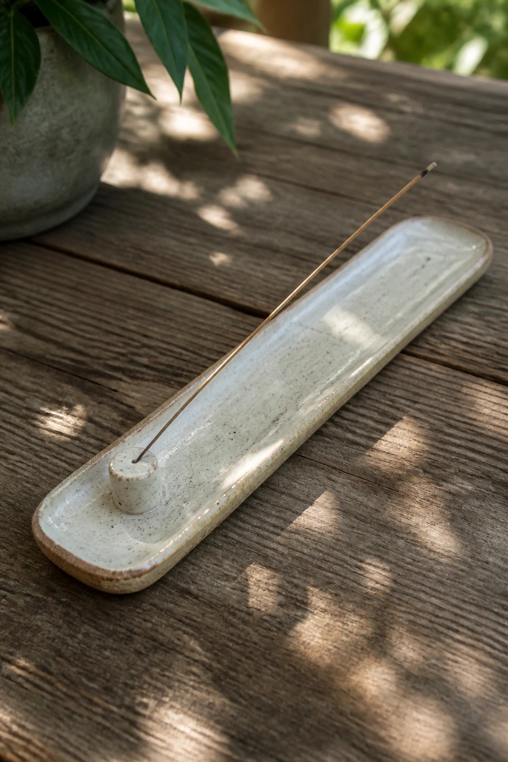 Ceramic incense holder with thin stick on sunlit wooden table near plant