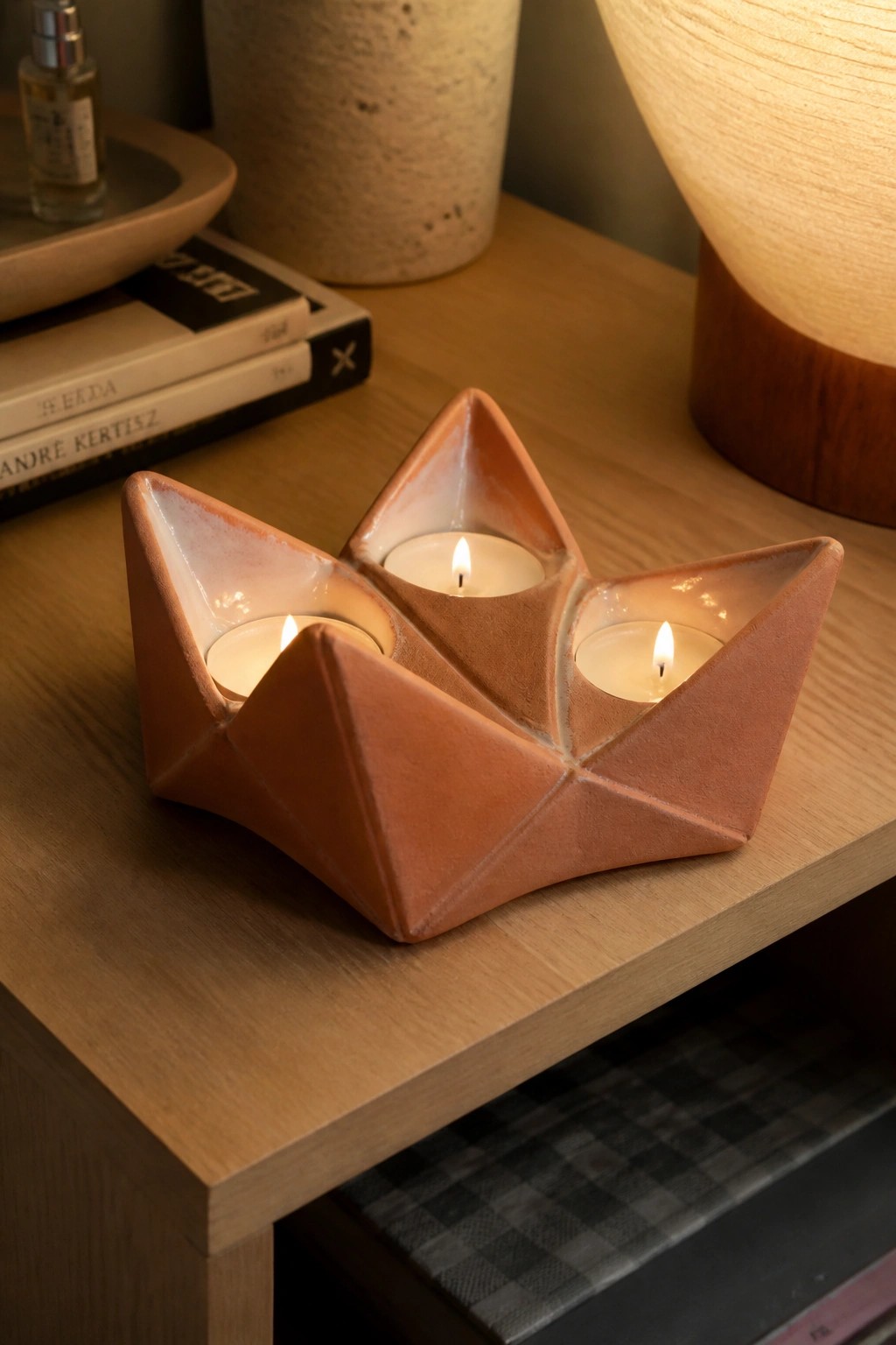 Geometric terracotta holder with three lit candles on wooden table