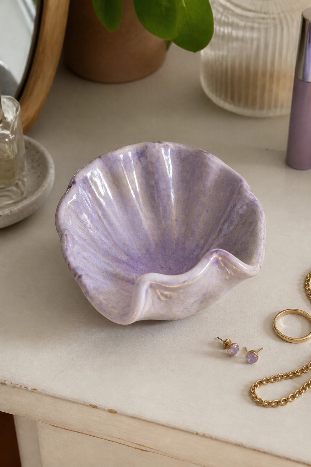 Purple shell-shaped ceramic bowl beside gold jewelry and amethyst earrings on table