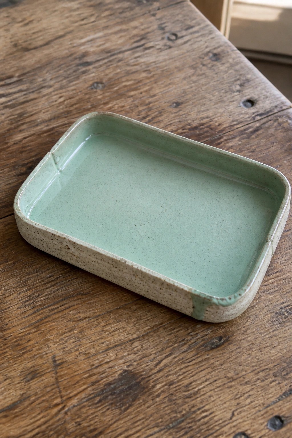 Rectangular speckled ceramic tray with light green glaze on wooden table