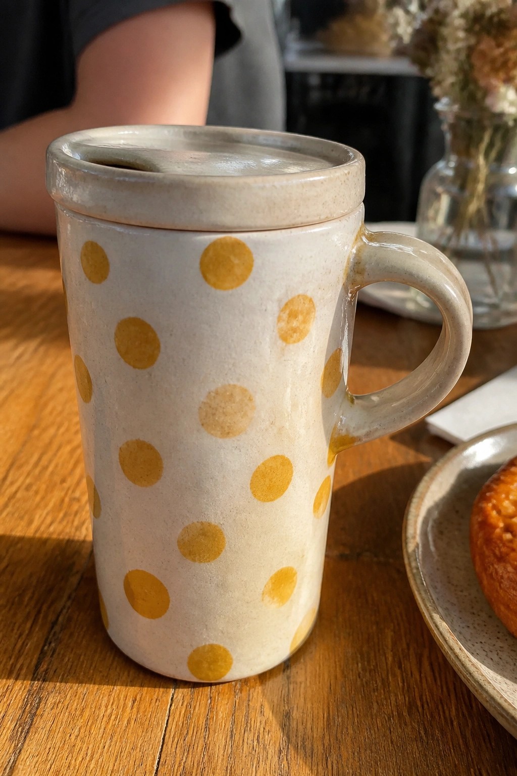 Cream ceramic mug with yellow polka dots and lid on wooden table