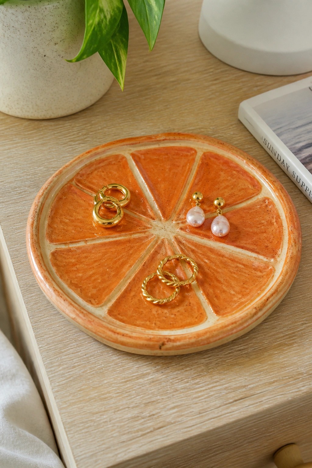 Orange ceramic slice plate with gold hoops and pearl earrings on wooden table