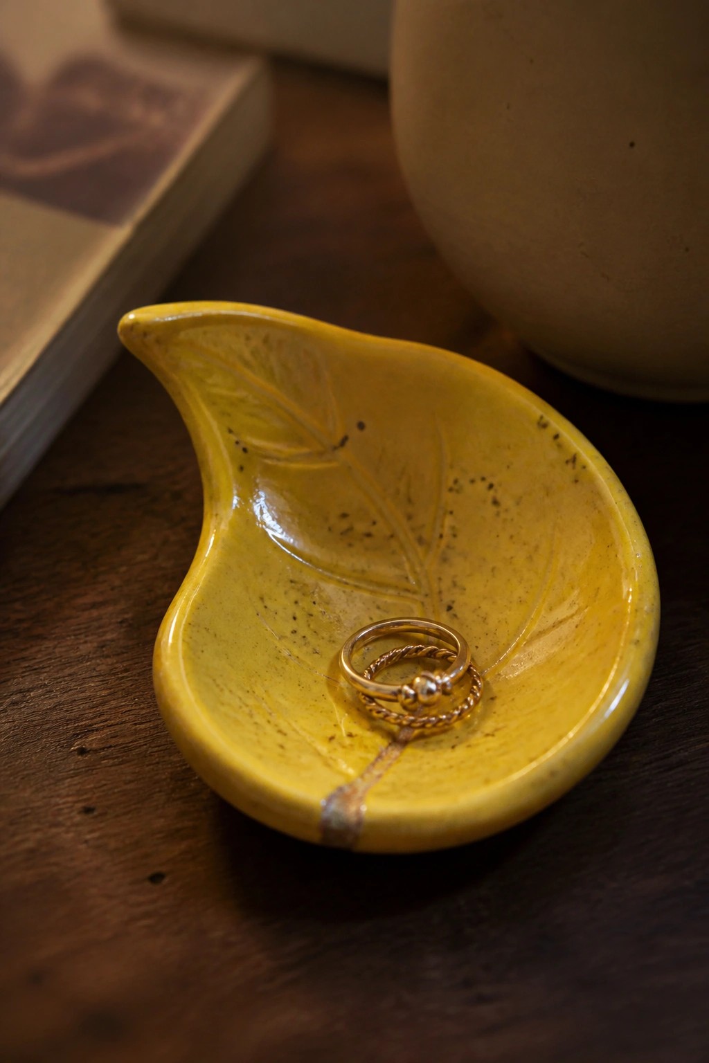 Yellow ceramic leaf dish holding two gold rings on dark wood
