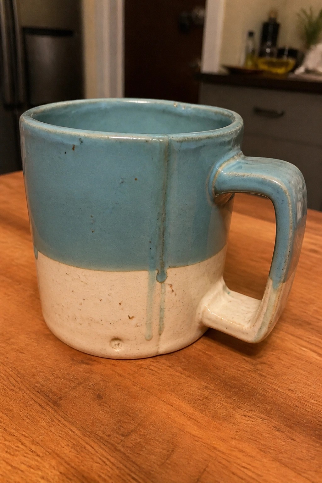 Light blue and white ceramic mug with dripping glaze on wooden table