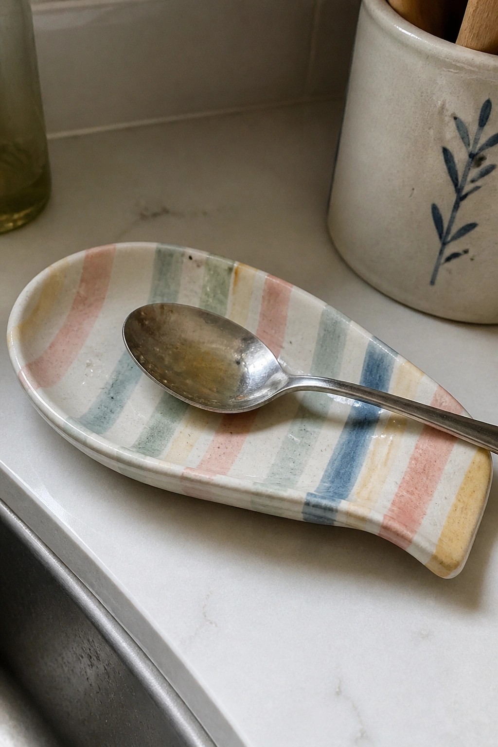 Tarnished spoon on pastel striped ceramic rest atop white marble countertop