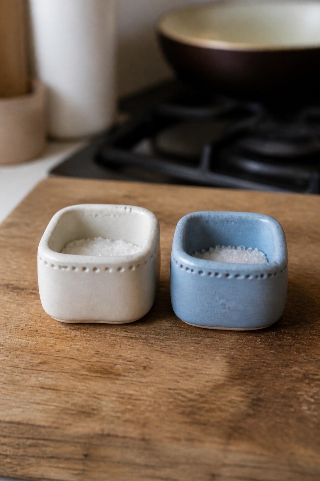 Two ceramic bowls, white and blue, filled with salt on wooden board