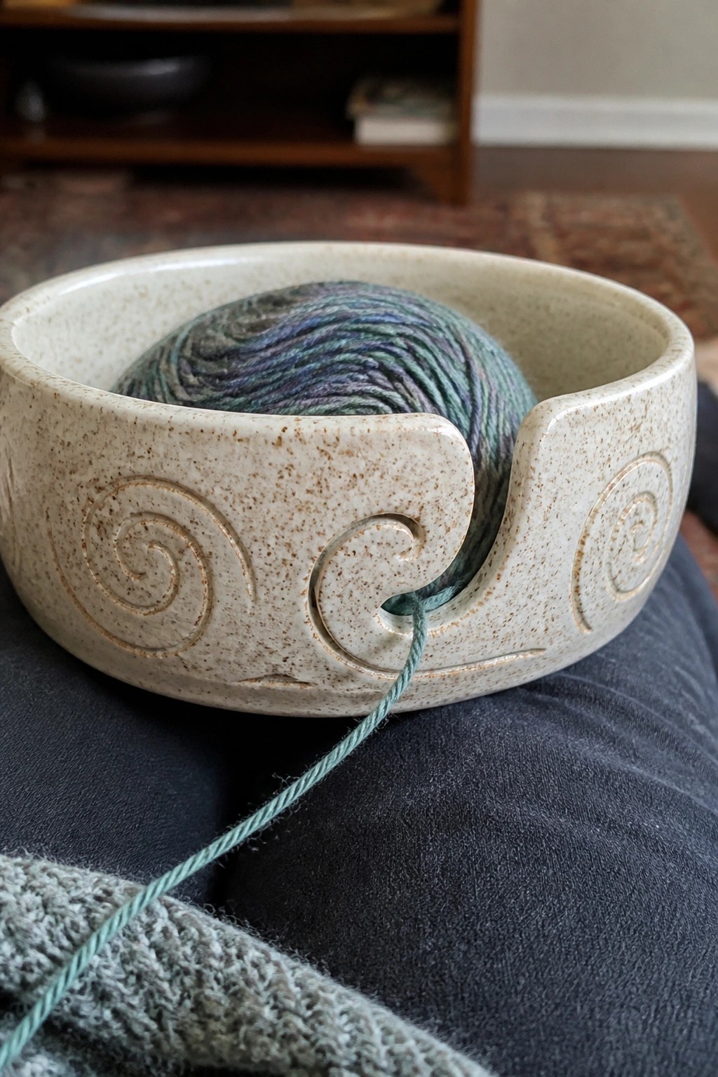 Speckled ceramic yarn bowl with spirals holding variegated yarn on dark fabric lap