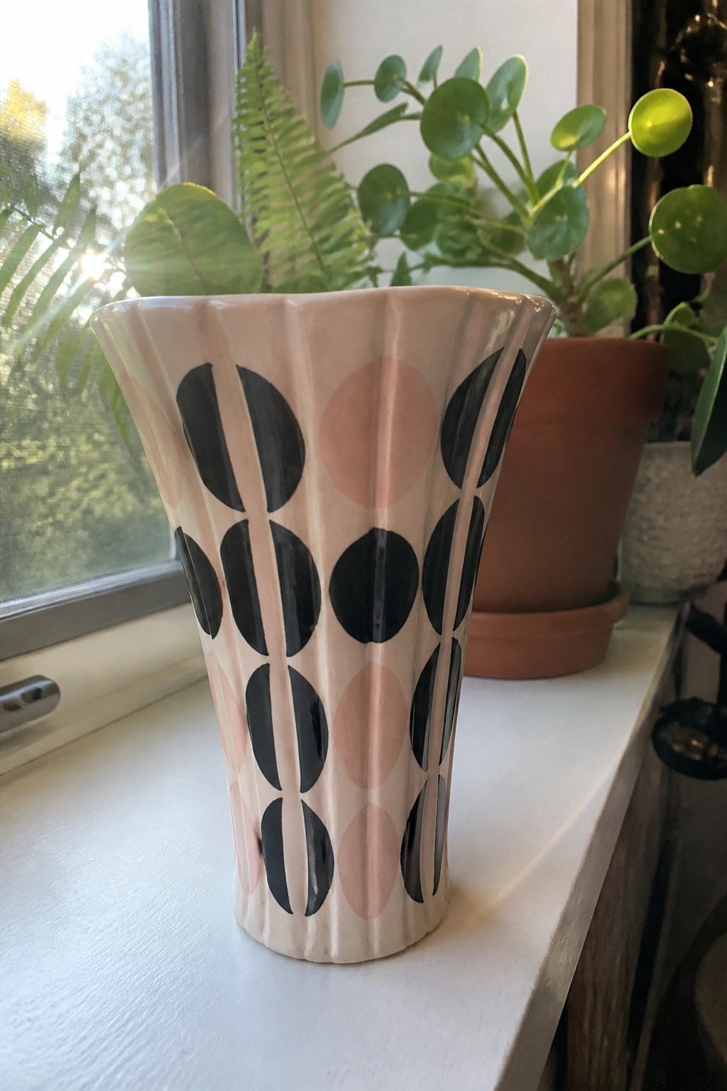 Pink fluted vase with black and pink dot pattern on sunny windowsill