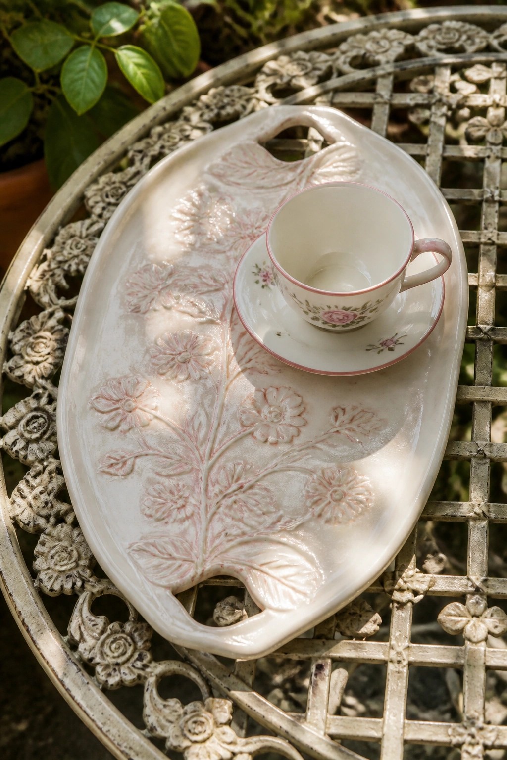 White ceramic tray with embossed flowers holding pink rose teacup on metal table