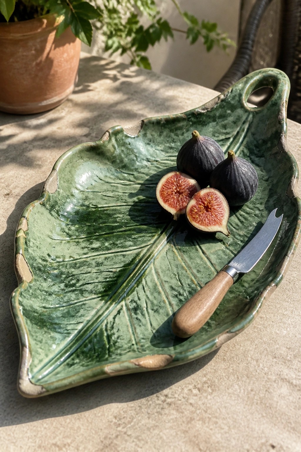Green leaf-shaped ceramic tray holding whole and halved figs with a small knife.
