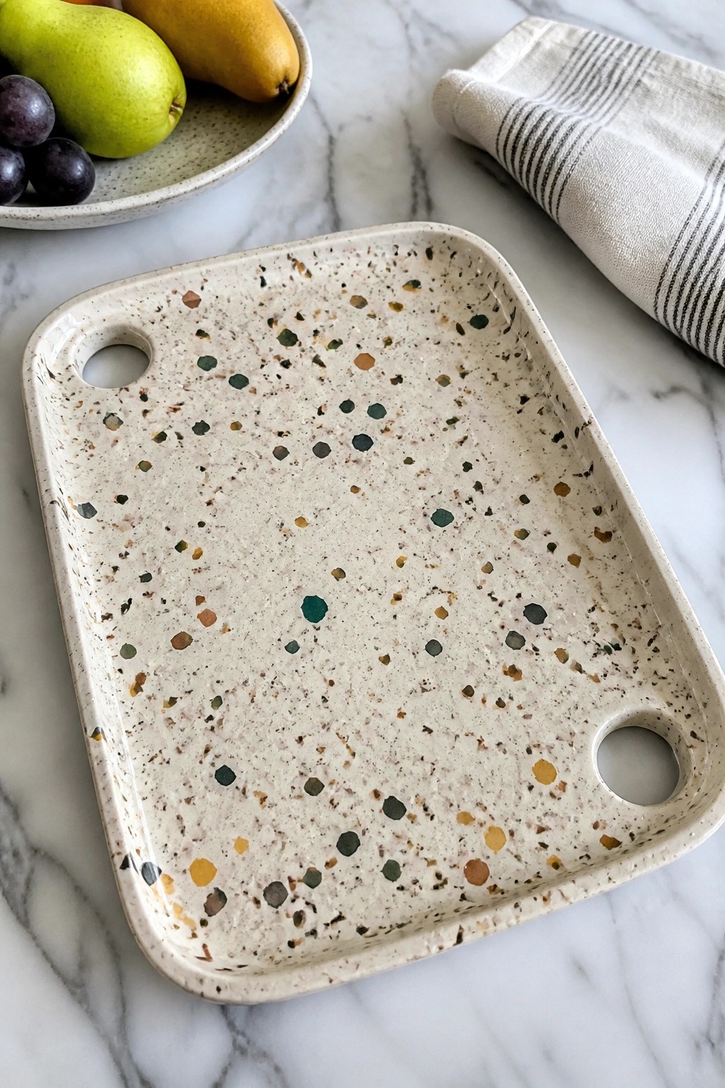 Cream speckled tray with handles on marble near fruit bowl and striped cloth