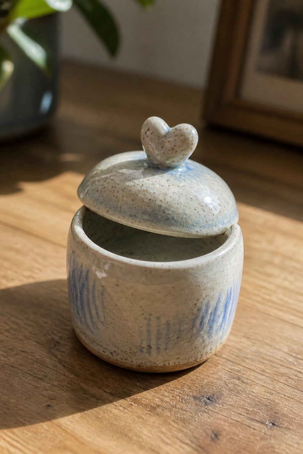Speckled ceramic jar with heart knob, lid slightly ajar on wooden table.