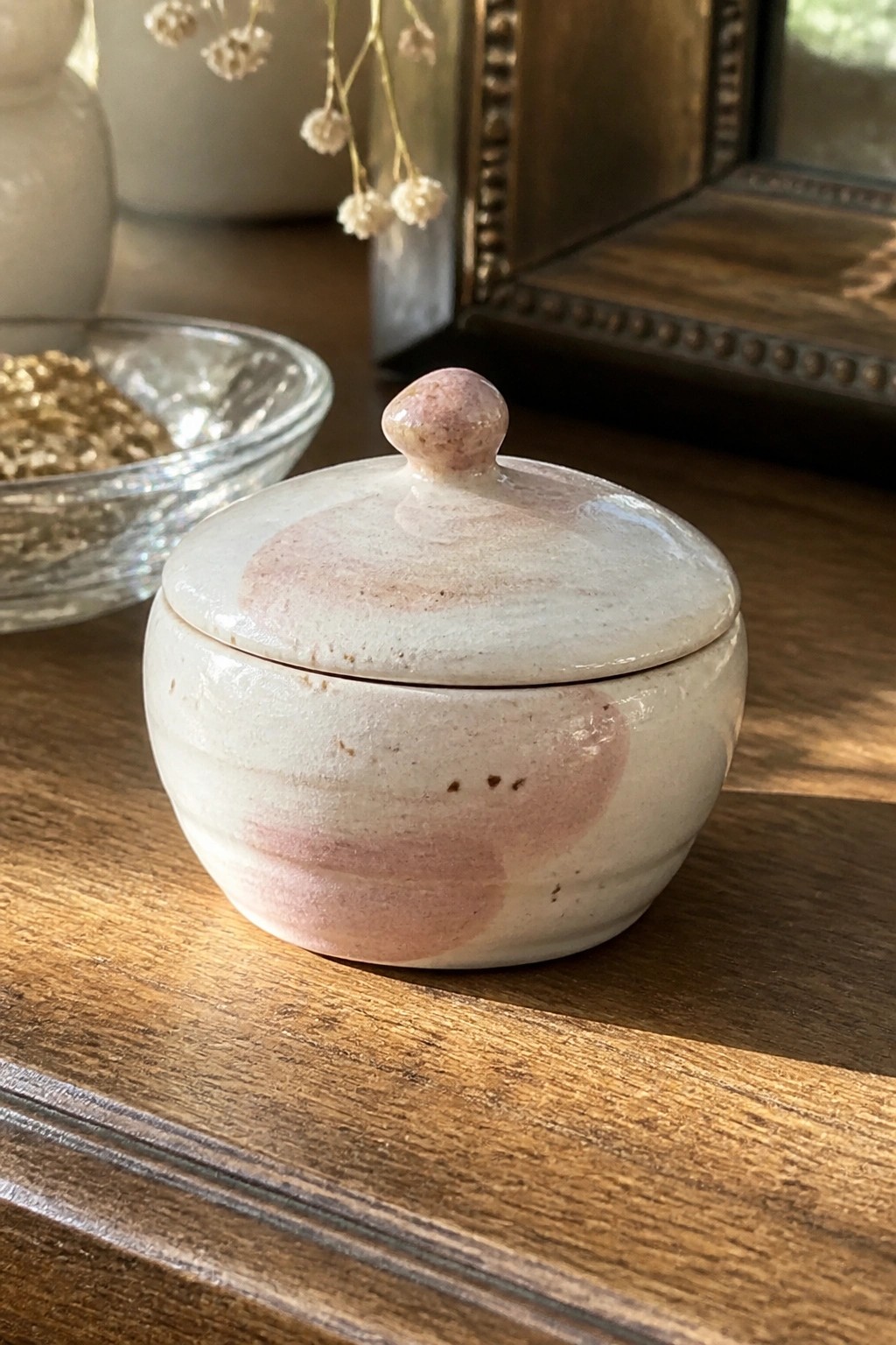 Small ceramic lidded jar with pink-swirled white glaze on wooden table