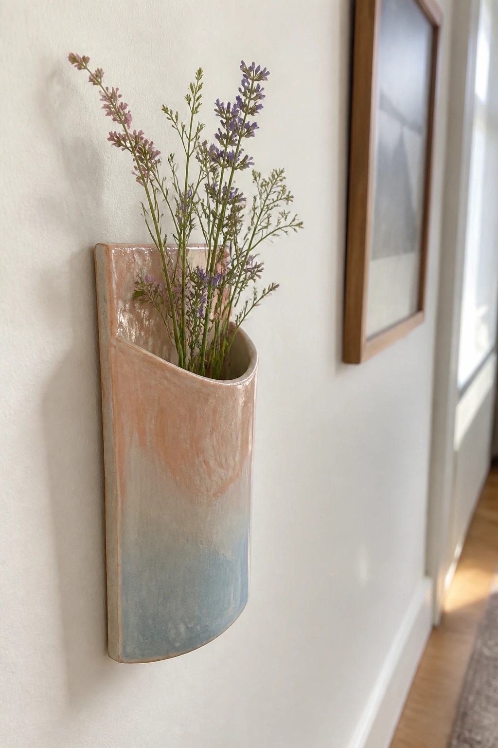 Peach-to-blue ceramic wall vase holding purple dried flowers on white wall