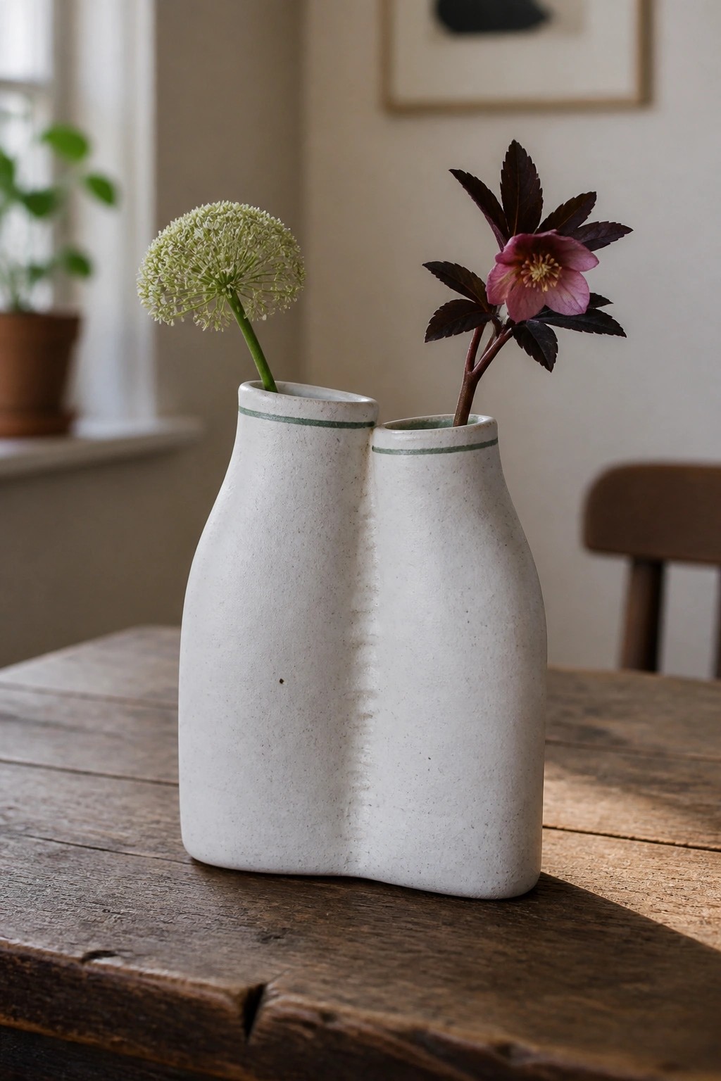 Speckled white double ceramic vase with green trim holding pink and green flowers on wood table