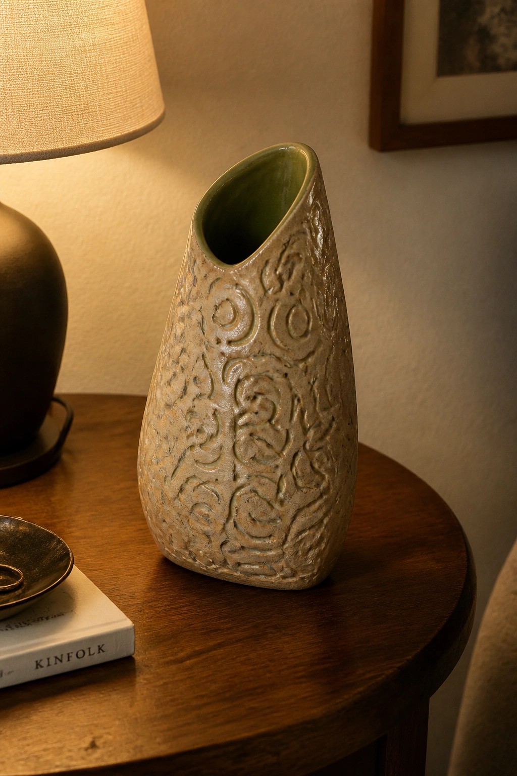 Textured ceramic vase with embossed patterns on round wooden table beside lamp