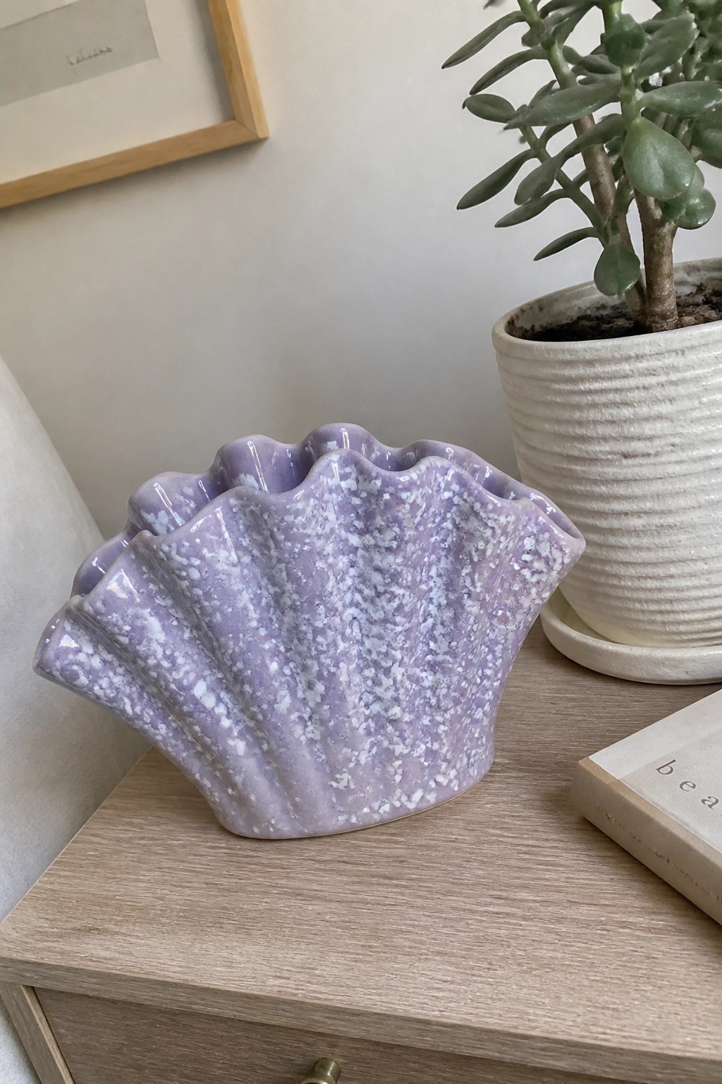 Speckled lavender scallop-shell ceramic vase on wooden table beside potted plant