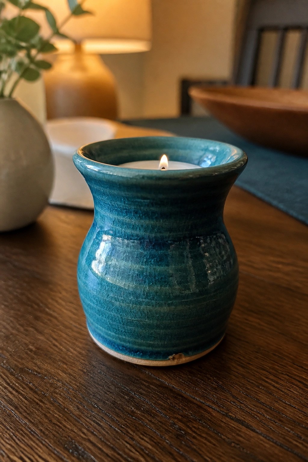 Lit teal crackled ceramic candle holder with flame on wooden table