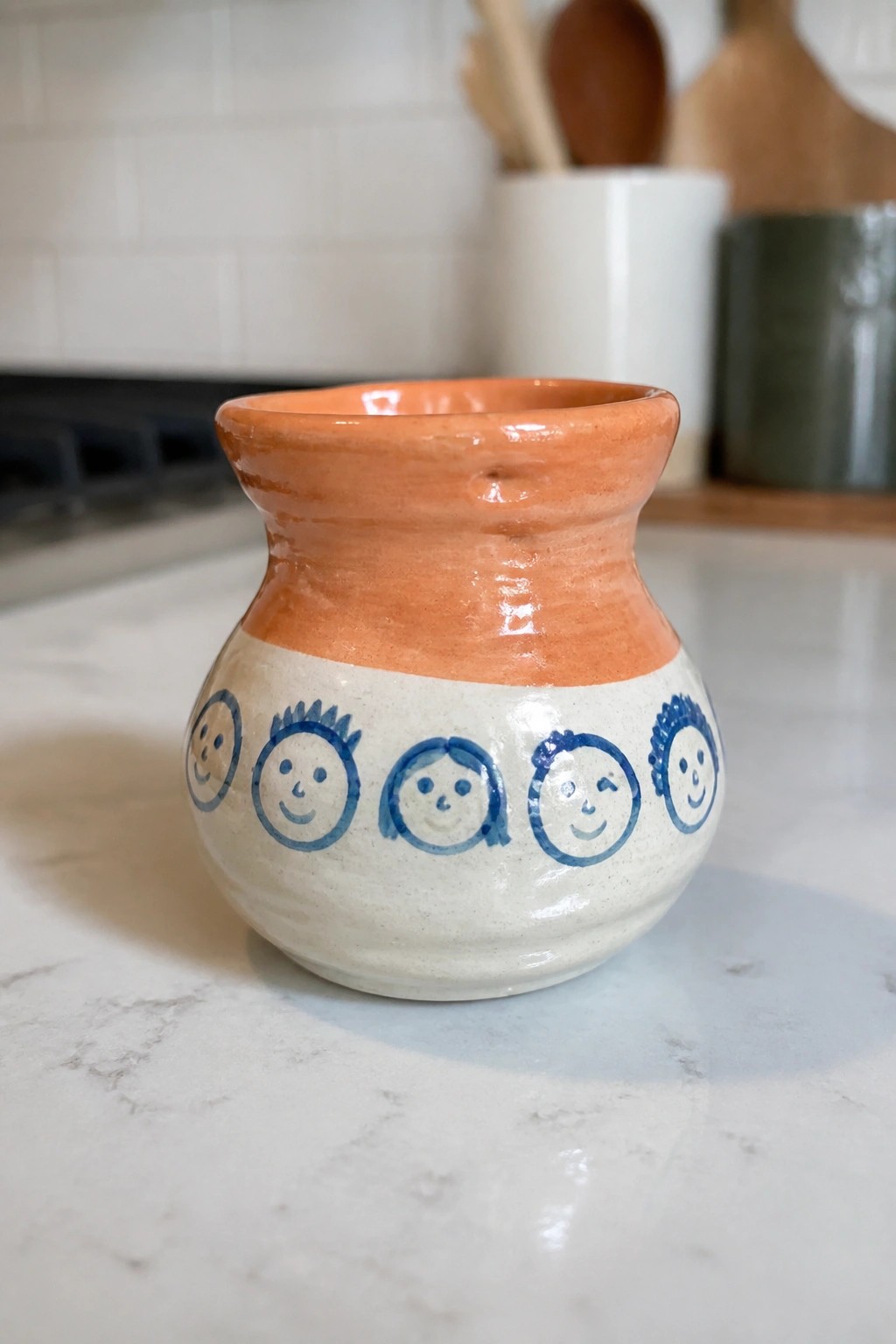 Ceramic pot with orange rim and blue smiling faces on white body