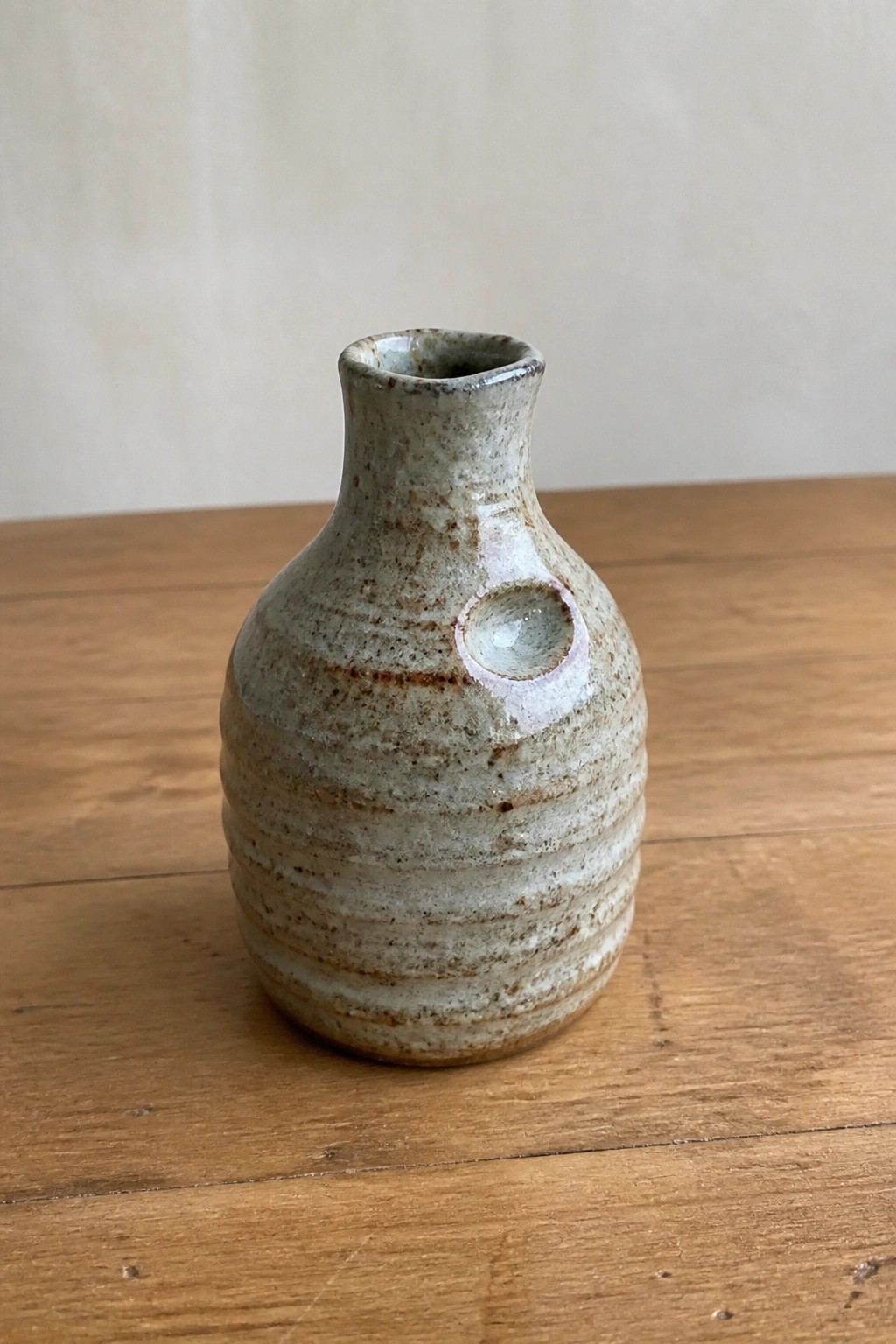 Small speckled ceramic vase with side hole on wooden table