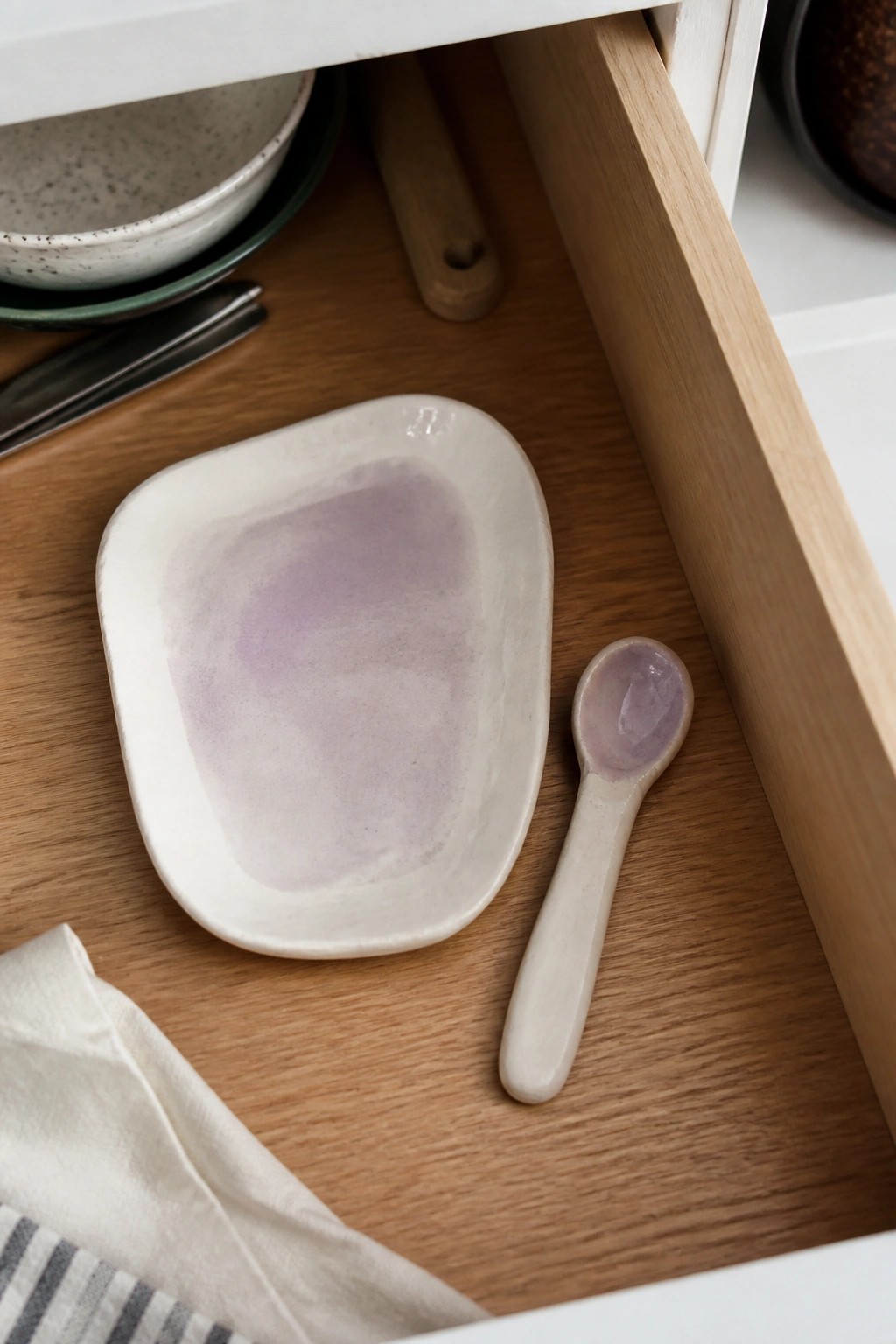 Open wooden drawer holding white-purple ceramic dish, spoon, and kitchenware